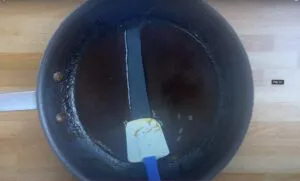 Non-stick pan with pan sauce, scraped by spatula on a wooden surface, showing thick consistency.